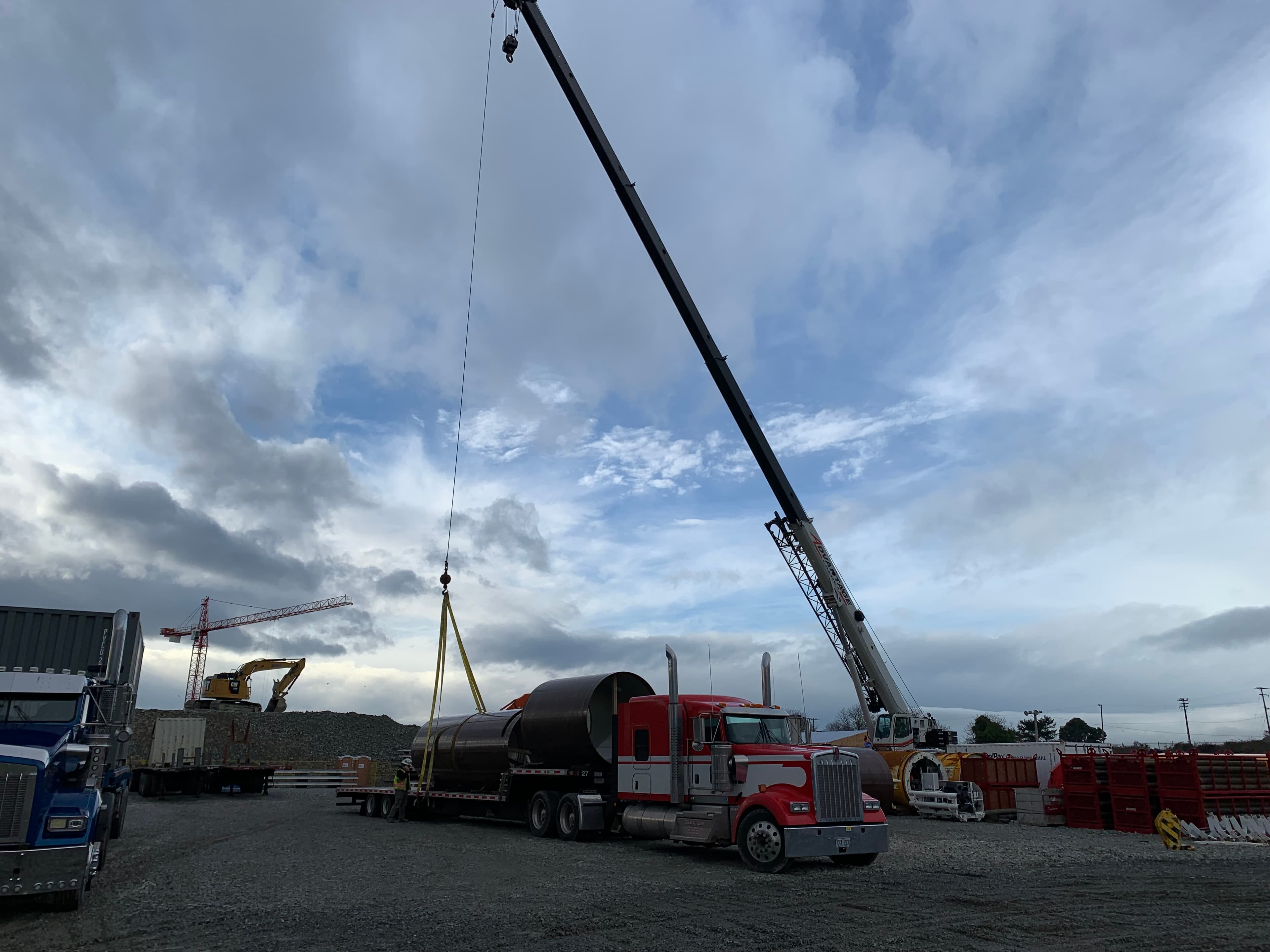 Crane loading a large cylindrical pipe onto a Stein & Sons RGN trailer