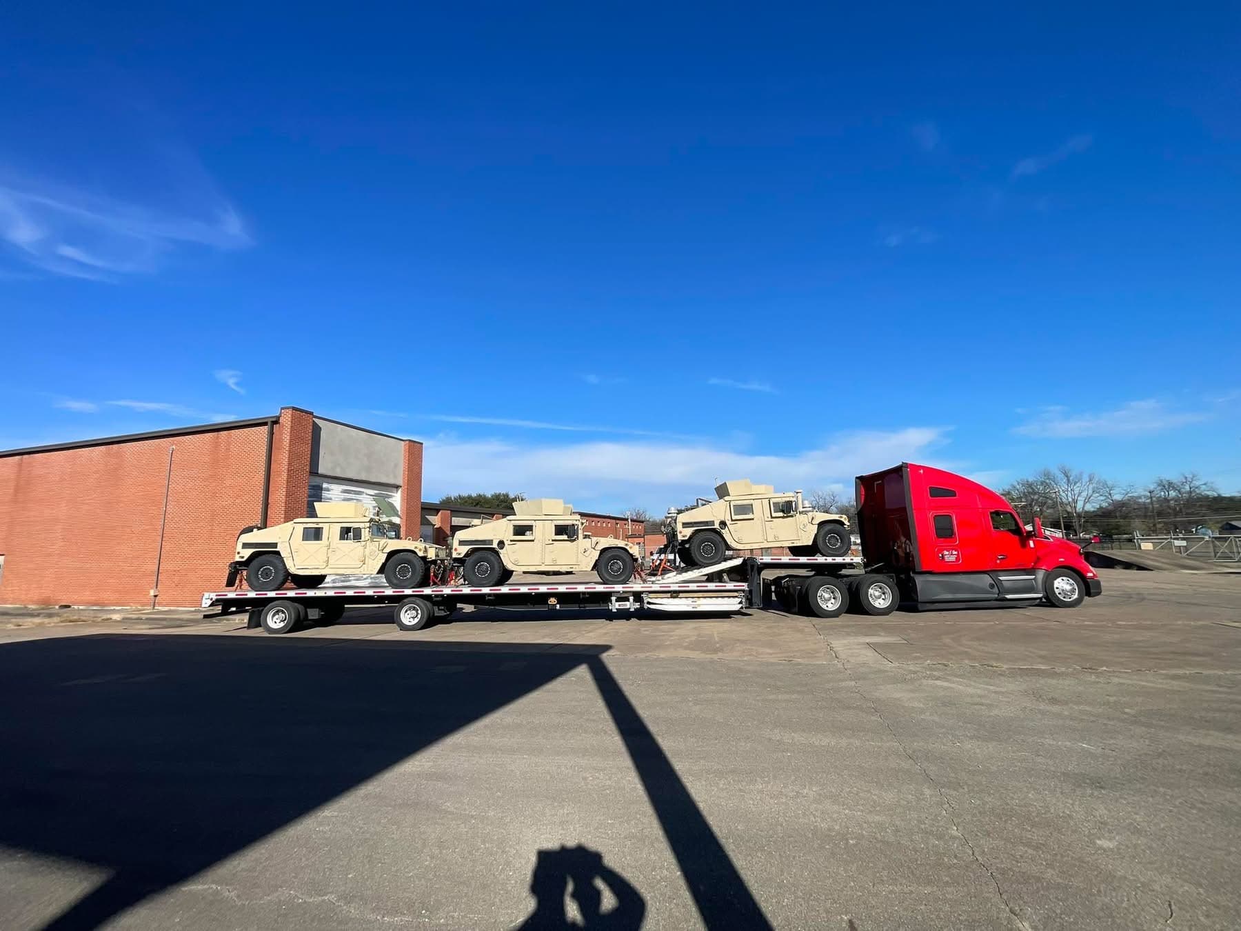Step deck trailer with three secured Humvees